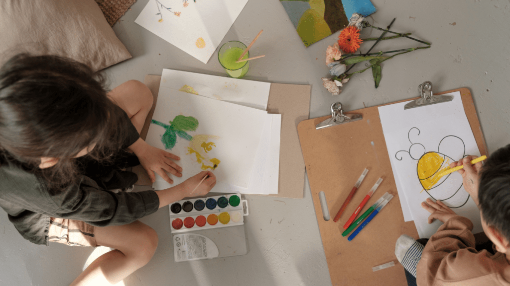 Two children are sitting on the floor and drawing with crayons