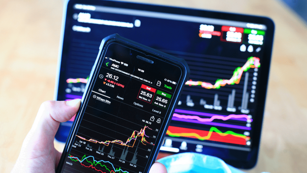 a person holding a smartphone in front of a computer screen displaying stock market data