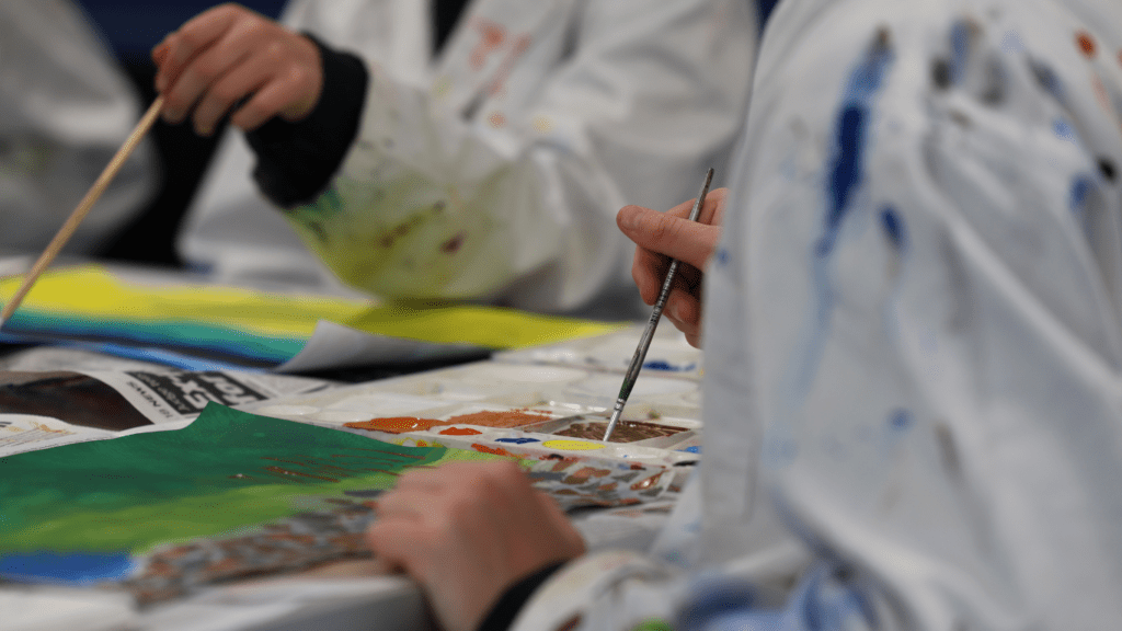 a group of people sitting at a table with watercolors and paintbrushes