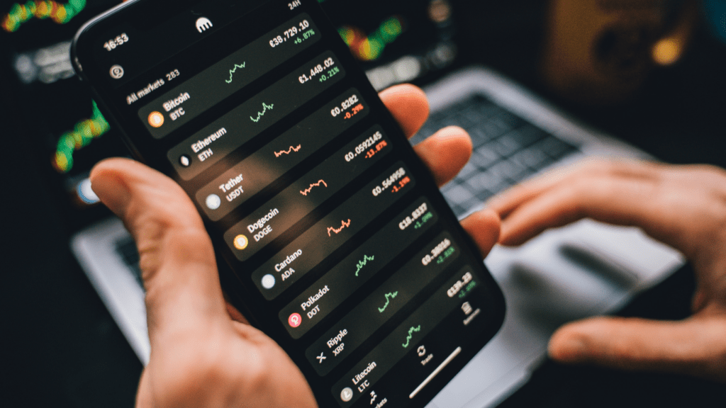 a person holding a smartphone in front of a computer screen displaying stock market data