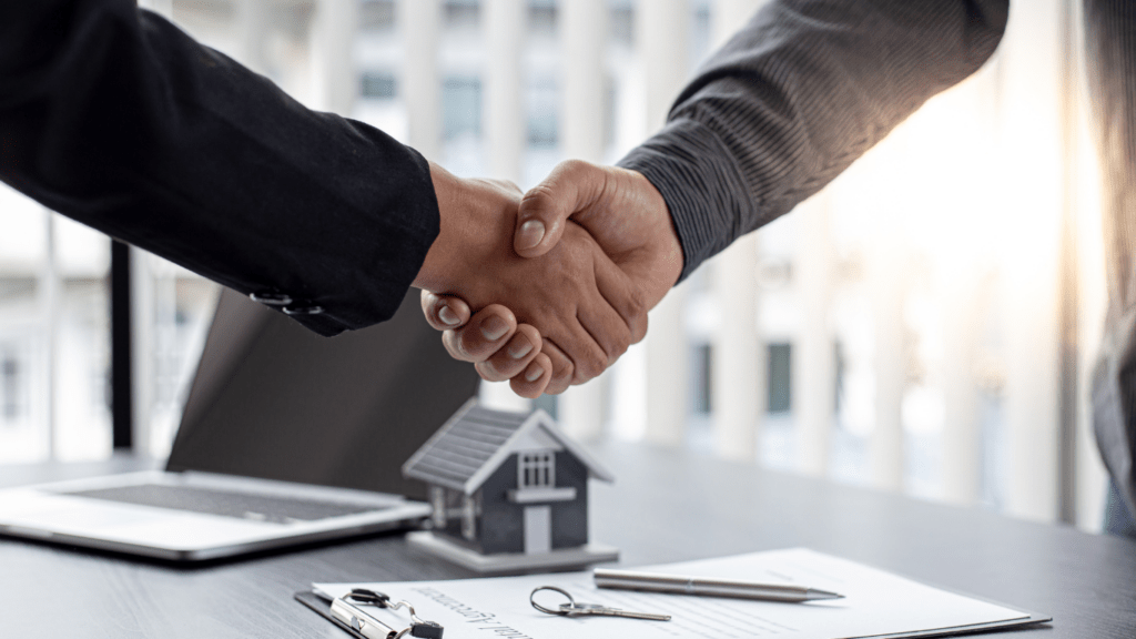 two people shaking hands over a house model on a desk